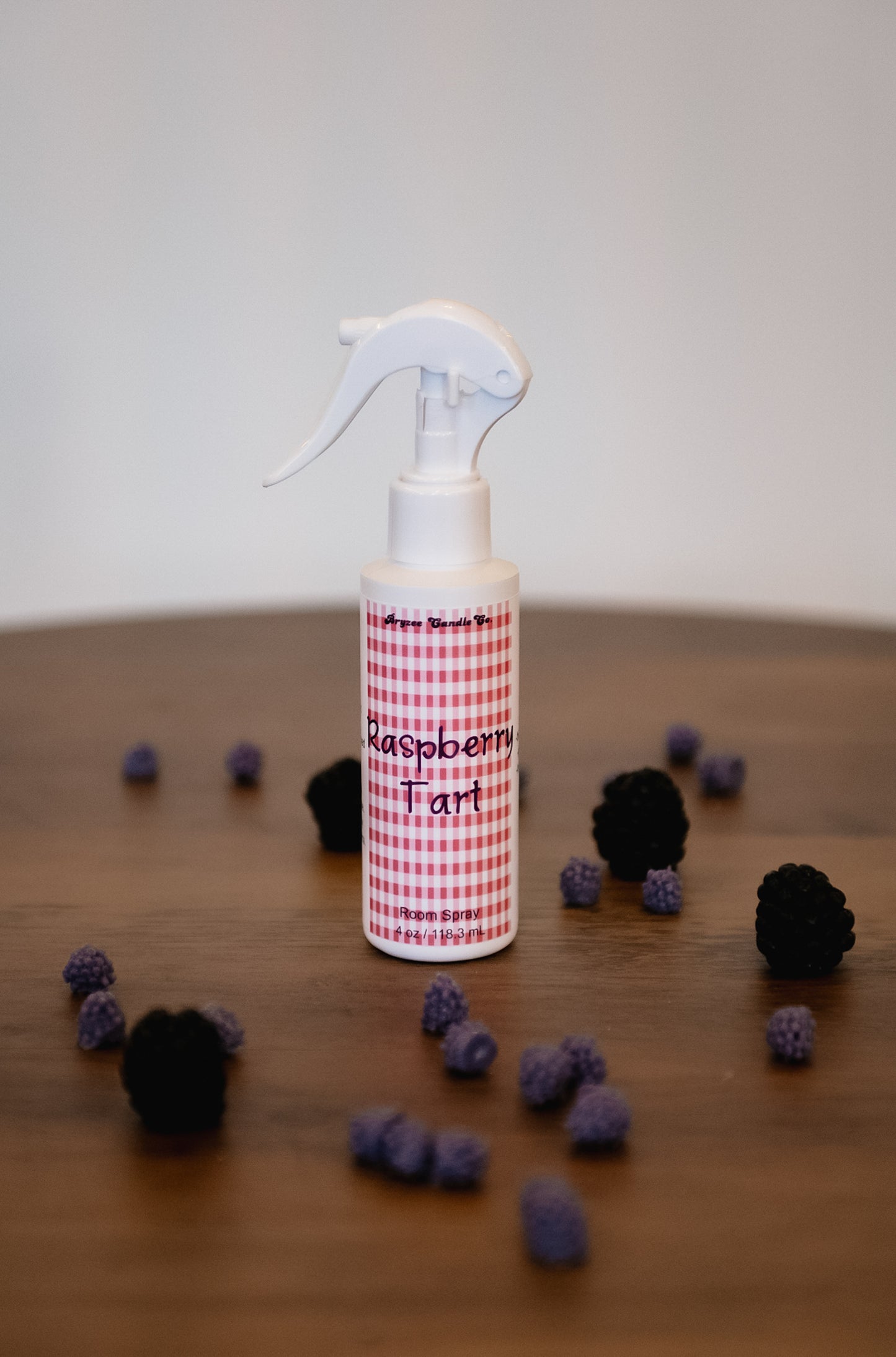 Spray bottle labeled 'Raspberry Tart' on a wooden surface with black and purple berries around it.