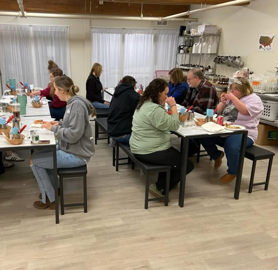 A group of people seated at small tables eating and talking during a candle-making class in Massachusetts